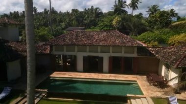 Beyaz kumlu plaja erişimi olan okyanus kıyısındaki lüks retro villanın insansız hava aracı videosunu alıyoruz. Sri Lanka tatil köyünde yüzme havuzu ve palmiye ağaçları olan kır evinin dış görünüşü.