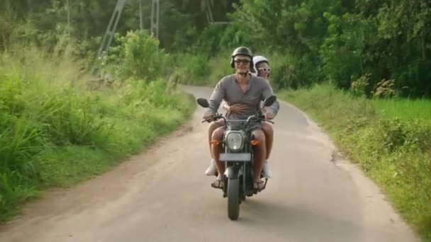 快乐的年轻夫妇骑摩托车旅行 两个快乐的情人在丛林中路上骑摩托车 女朋友笑了 张开胳膊 游客在日落时驾驶摩托车 男人和女人的旅程冒险 — 图库视频影像