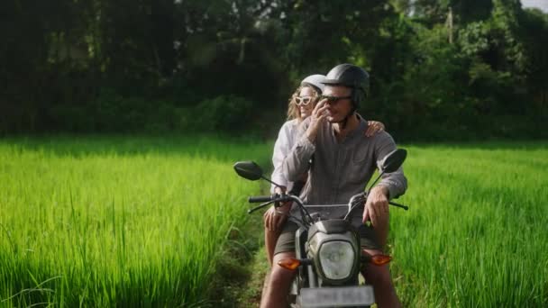 夫妻在稻田里骑摩托车聊天 恋爱中的女人骑自行车在热带地区 停下来看丛林种植园 骑摩托车旅行的愉快游客 女孩用手指向凉爽的景色 — 图库视频影像