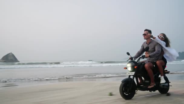 黄昏时 旅客们骑摩托车沿着沙滩行驶 女人驾驶摩托车在热带岛屿海岸线 女朋友抱着男朋友 张开双臂 笑着庆祝骑自行车的自由 — 图库视频影像