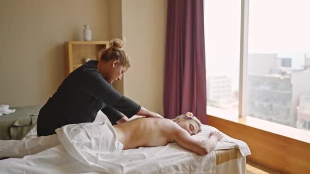 多民族按摩师为年轻的金发女性做了一次康复性的背部按摩 部分覆盖着白色的毯子 Biracial Spa中心的女雇员对病人实施良好的程序 — 图库视频影像