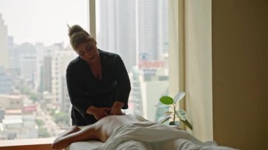 Çok ırklı masöz, lüks spa merkezindeki muhteşem manzaralı genç bayana nazikçe masaj yapıyor. Çift ırklı spa merkezi kadın çalışanı dinlenme tesisinde müşterilerine sağlık prosedürü uyguluyor..
