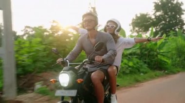 Motosiklete binen mutlu çift. Sevgililer gün batımında motosikletle gezerler. Aşık bir kadın orman yolunda coşkuyla el ele tutuşur ve bağırır. Güzel turistler bisiklet yolculuğunun tadını çıkarır. Güneş patlamaları
