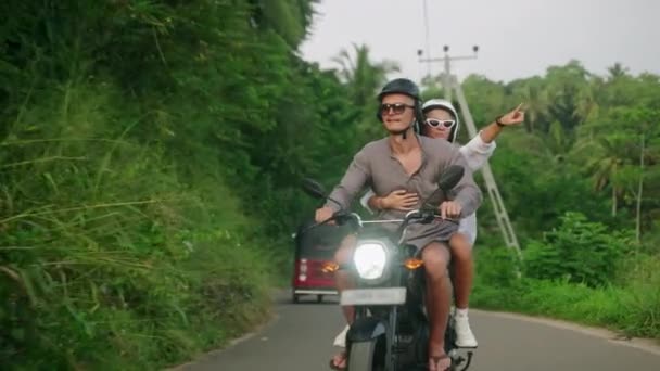 一对快乐的夫妇骑摩托车 两个情人骑摩托车在热带地区旅行 女朋友指指点点 男人驾驶摩托车在丛林里 游客们骑自行车探索不同的地方 女人喜欢冒险 — 图库视频影像