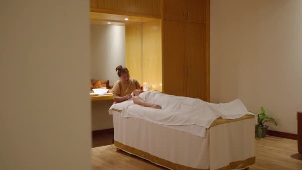 Senior Asian Beautician Does Facial Massage Jade Roller Female Client — Stock Video
