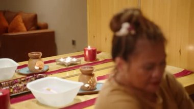 Odaklanmış Asyalı kadın spa merkezi çalışanı müşteri portresi çekimine odaklanmadan prosedür uyguluyor. Sağlık merkezindeki iki ırklı yaşlı bir masözün yakın çekimi. Mumlar, çiçekler ve güzellik aletleri.