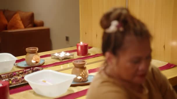 重点介绍了亚洲高级女疗中心工作人员对客户肖像照片拍摄无精打采的程序 在健康中心为一位双族老年女按摩师提供的服务 花和美容工具 — 图库视频影像