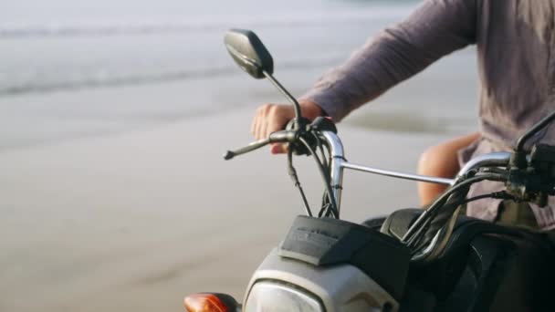バイカーはオートバイのハンドルバーを海辺に置く 人々は海岸でバイクのハンドルを保持しています バイクダッシュボード リアビューミラー 海岸のスクーターに座っている男 — ストック動画
