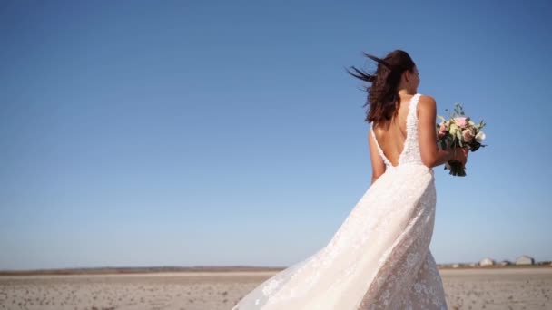 豪華なウェディングドレスの美しい女性は 砂漠の風景 風の強い天気で歩いています 結婚式の後 新鮮な花の花束とエレガンスの花嫁 魅力的なモデル — ストック動画