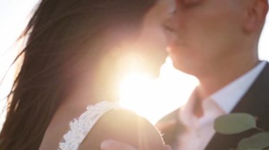 Yeni evliler, gün batımında romantik bir buluşmada açık havada şefkatle sarılıyorlar. Mutlu gelin ve damat balayında duygularını gösteriyor. Düğün gününde poz veren çekici erkek ve kadın. Yakın plan..