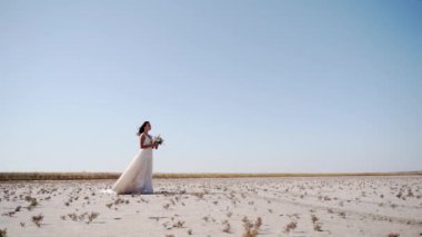 Çöl manzarasında narin bir buket tutan güzel bir gelin, rüzgarlı bir hava. Zarif bayan nikahtan sonra damadı bekliyor. Doğada muhteşem beyaz elbiseler içinde çekici bir model..