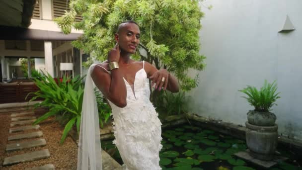 Lgbtq黑人穿着白色婚纱在热带花园靠近水百合池塘的地方假扮模特 同性恋的比波克新娘在常青树和豪华别墅的映衬下表现出美丽和温情 — 图库视频影像
