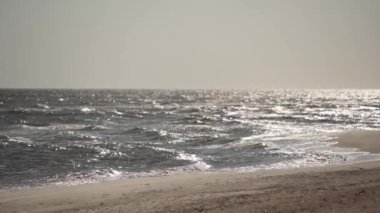 Kumlu kıyı şeridine düşen su dalgaları, güneşli hava. İnsanlar olmadan kıyı şeridi manzarası, yaz günbatımında deniz sörfü. Boş sonbahar plaj manzarası. Tatilde deniz kenarında rahatla..