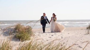 Gelin ve damat el ele tutuşup deniz kıyısında yürüyorlar. Takım elbiseli çekici bir adam, gelinlik giymiş bir kadın kumsala gider. Aşık çift düğün töreninden sonra romantik fotoşoplar çekiyor..