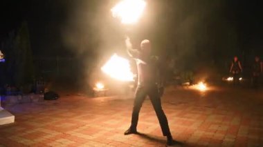 Yangın gösterisi. Erkek sanatçı geceleri yanan ateş fanlarıyla hokkabazlık yapıyor. Siyah elbiseli bir adam festivalde ateşle gösteri yapıyor. Ateş dansçısı karanlıkta yanan kazıkları çevirir.