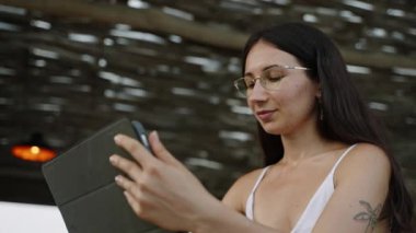 Sazdan çatılı bir restoranda çalışan genç bir kadın. Tropikal kafede uzaktan çalışma için tablet kullanan SMM yöneticisi. Seyahat blogcusu kafede video blogu düzenliyor. Okyanus kıyısındaki barda oturan serbest çalışan.