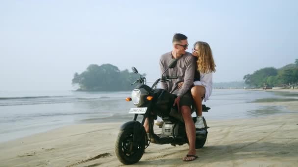 恋爱中的女人骑摩托车坐在海边 享受日落 女友拥抱 看男人在海上骑摩托车 新婚夫妇度蜜月时喜欢看照相机 — 图库视频影像