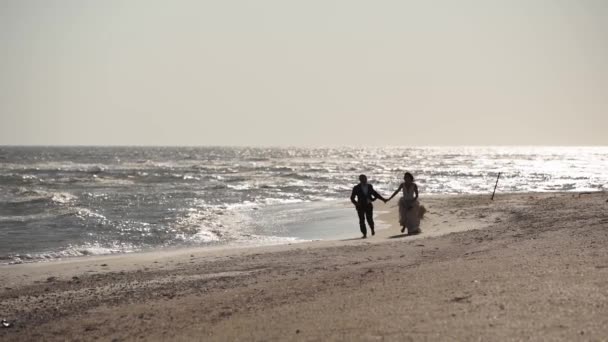 結婚式の写真撮影で砂浜の海岸を走る夫婦と結婚したばかり ビーチで楽しむ花束と花嫁 風に振る豪華な白いドレス — ストック動画