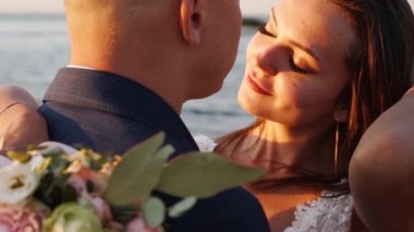 Yeni evliler sarılıyor, düğün günü deniz kıyısında öpüşüyorlar. Muhteşem dantel elbiseli gelin, deniz kenarında güneş doğarken poz veren damat. Romantik fotoşoplara sarılan evli bir çift..