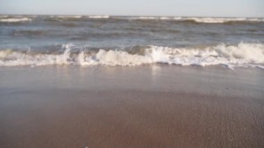 Kumlu kıyıya düşen sinematik köpüklü dalgalar. Su yüzeyi dokusunun inanılmaz deniz manzarası. Kum gün batımında dalgalarla yıkanır. Deniz kenarında yaz tatilinin tadını çıkar. Yakın plan..