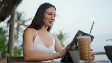Kadın serbest yazar, kafeteryada, okyanus manzaralı, palmiye ağaçlı grafikler tabletinde stilus ile resim çizer. Sanatçı kız deniz kenarında cihaz üzerinde çalışıyor. Tropikal adada uzak çalışma gününde genç illüstratör.