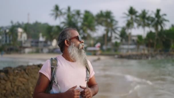 灰色のひげの旅行を持つ男は ヤシの木 暖かい海と砂浜と熱い南国のシニアライフをお楽しみください 高齢者はリラックスした場所 瞑想的な休日 落ち着いた退職を求めます — ストック動画