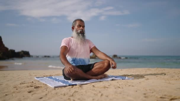 年长的灰胡子旅行者使用冥想练习和瑜伽来净化心灵 坐在热带岛屿上的荷花姿势 上了年纪 闭着眼睛 享受着退休生活 享受着棕榈树和大海 — 图库视频影像