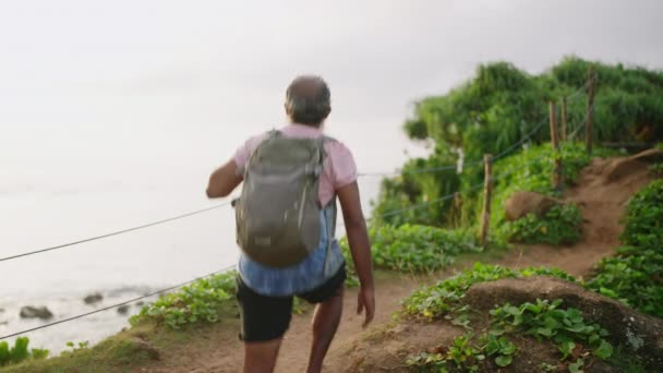 老人爬上石阶 手持木绳扶手爬到斗篷顶上 长有灰胡子的老年人在热带度假旅行中游览自然景观 老男性探险岛 — 图库视频影像