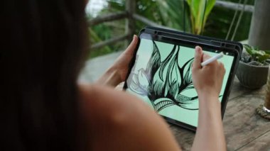 Kadın çizer elleri tablet üzerinde okyanus manzaralı, palmiye ağaçları. Deniz kenarındaki terasta çalışan serbest çalışan biri. Güzel kadın cappuccino içer. Yakın plan, arka plan.