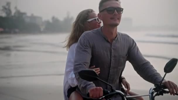 浪漫的夫妻在日落时骑摩托车在海滩上约会 情侣们骑摩托车在海岸线上旅行 女友拥抱男友 张开双臂 享受蜜月之旅 人们会留下一个框架 — 图库视频影像