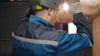 Güvenlik giysisi ve koruyucu maskeli profesyonel kaynakçının yakın çekimi inşaat alanının duvarına metal kaynak yapmaya başlar. Genç işçi çalışma sürecine hazırlanıyor.