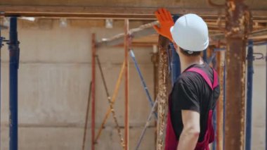 Yatay biçimlendirme çalışmalarını kontrol etmek için inşaat sahasında inşaat iskeleti arasında Hard Hat giyen Profesyonel İnşaat İşçisinin yan çekimlerinin ardından