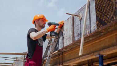Profesyonel inşaat işçisinin sabit şapka ve önlükle yan görüntüsü, daha fazla beton dökülmesi için elektrikli tornavidayla biçimlendirme yapıyor