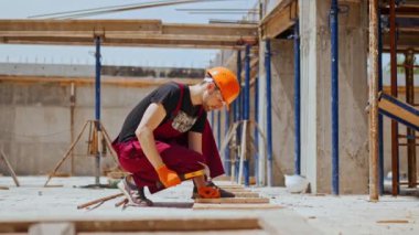 Profesyonel inşaat işçisinin inşaat alanındaki pervazlara çivili çekiçlerle çivili önlük giyip çekiçle otururken çekilmiş bir fotoğrafı.