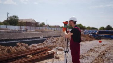 Profesyonel İnşaat İşçisi Teodolit Araştırması Optik Enstrüman Kullanıyor. Sert şapka ve önlük giyen adam bina planlarının açılarını ölçüyor