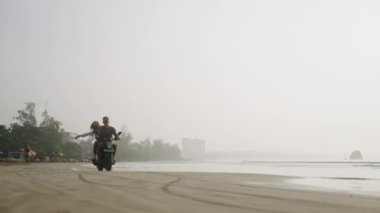 Gezginler motosiklet sürerler, gün doğumunda kumlu sahil kenarından geçerler. Kadın, erkek, tropik ada kıyılarında motosiklet kullanıyor. Kız arkadaş bir erkek arkadaşı kucaklıyor, kollarını açıyor, gülüyor..