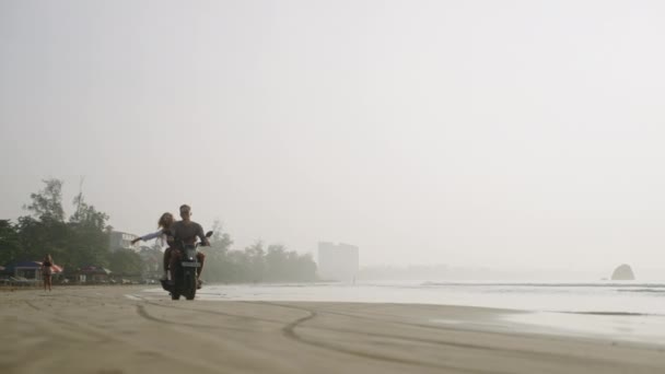 旅行的夫妇骑摩托车 日出时在沙滩上经过 女人去骑摩托车在热带岛屿的海岸线 女朋友拥抱男朋友 张开双臂 — 图库视频影像