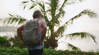 Yaşlı siyah adam tepedeki turistik yerden hayran olunan manzarayı görmek için egzotik bitkilere, çiçeklere ve palmiye ağaçlarına gidiyor. Gri saçlı yaşlı turist adanın okyanus manzarasının tadını çıkarıyor.