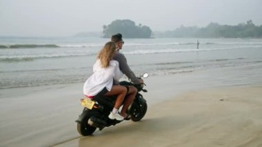 Gençler gün doğumunda deniz kenarında motosiklet sürerler. Okyanus kıyısında motosiklet süren bir kadın. Bikinili, tişörtlü, güneş gözlüklü güzel bir kız kameraya dönüp gülüyor, el kaldırıyor. Rüzgar saç savuruyor..