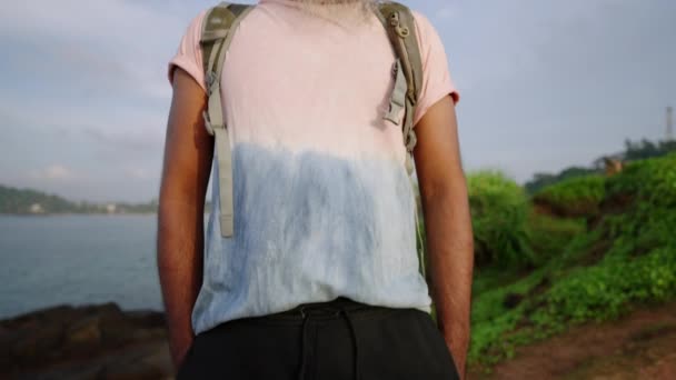 穿着T恤衫 背着灰胡子日光浴的时髦帅气老人 带着大海 地平线 异国情调的自然和植物欣赏着热带岛屿的美景 退休旅行人员的生活 — 图库视频影像