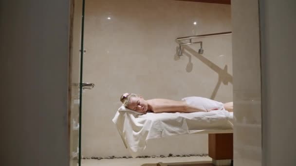 女人躺在洗澡间的床上 女性放松在桌上准备好身体皮肤治疗 在桑拿浴室中通过擦拭 剥皮按摩的方式进行抗衰老和抗蜂窝化治疗 — 图库视频影像