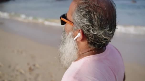 老年人在岸上用耳机跑步 观察健身追踪器的活动 卡路里 黑人男性在海滩慢跑 在退休的黄金岁月里带着远眺大海的景象享受运动生活 — 图库视频影像