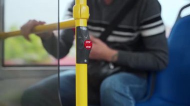 Yakından çekim yapan adam hareket halindeki otobüsteki tırabzanda kırmızı dur düğmesine basmak için ayağa kalkar. Adam, sürücünün toplu taşımadan çıkması için işaret vermek için düğmeye basıyor.
