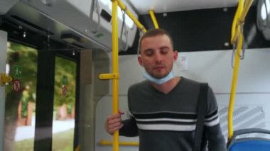 Genç erkek yolcu, tıbbi maske takarak tramvayla seyahat ediyor. Günlük kıyafetli bir adam akıllı telefona bakar, oturur ve kendini korumak için kişisel koruyucu giysiler giyer..
