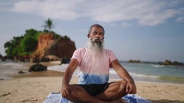 Yaşlı adam, okyanus kıyısındaki cennet adası sahilinde meditasyon yapıyor ve lotusta oturuyor. Zenci erkek kıdemli erkek yoga yaparken bacak bacak bacak üstüne atmış..