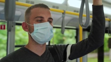 Tıbbi maske takmış, elinde tırabzan taşıyan genç bir yolcunun tramvay yolculuğu görüntülerini yakından çek. Günlük kıyafetler giyen Avrupalı adam toplu taşımacılıkta covid-19 'dan korunuyor.