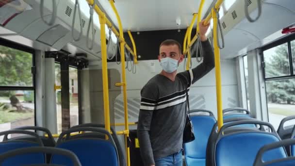 手持扶手戴着医疗面罩的年轻男性乘客准备在下一站公共汽车上下车 便衣人员在公共交通中受到保护 不受Covid 19伤害 — 图库视频影像