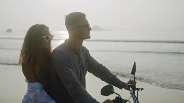 恋爱中的女人骑摩托车坐在海边 享受日落 女友在海上拥抱 亲吻骑摩托车的男人 新婚夫妇度蜜月 享受热带岛屿度假 — 图库视频影像