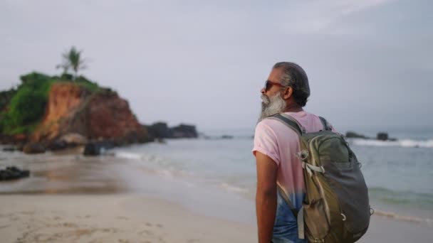 老黑人 背着背包走路 徒步旅行 环视热带岛屿上的海滨 老年男性旅行者享受退休旅行的异国情调海滩与蓝色的水 天空和发送 — 图库视频影像