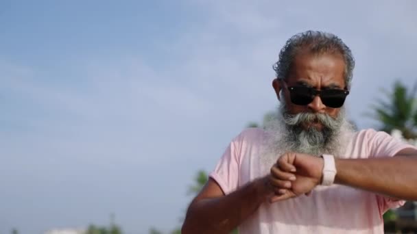 老年长跑者白胡子检查健康状况 使用现代健美跟踪器观看可佩带的小玩意 做运动慢跑活动 成年男子前往热带岛屿和海滩 — 图库视频影像